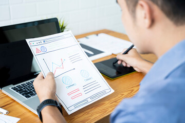 Fototapete - Working from home web designing graphical user interface UX UI, home office using computer laptop and pen sketching graphics tablet, using draft ideas and plans on paper drawing, asian man quarantine