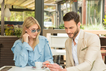 Attractive young couple drinking coffee and watching smart phone in garden restaurant