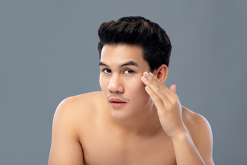 Close up portrait of young handsome Asian man touching his face to check wrinkles isolated on gray background for skin care and beauty concepts