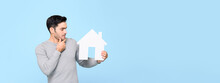 Young Man Looking At House Model And Thinking Isolated On Light Blue Banner Background With Copy Space