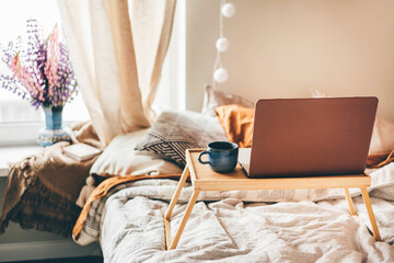 Wooden tray with coffee and laptop on bed.