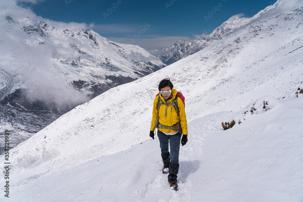 Young Asian woman trekking in Langtang valley after heavy snow storm. A woman trekking on trail that covered by fresh snow. Himalaya mountains range, Nepal - obrazy, fototapety, plakaty 