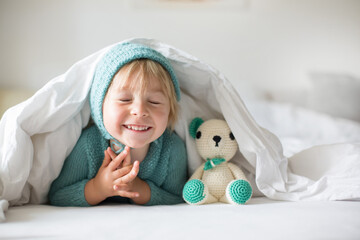 Canvas Print - Cute toddler boy with handmade knitted toy, lying in bed