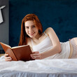 © Dmitrii Kotin - Young redhead woman lying and relax on the bed and looks in her diary