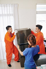 Wall Mural - Unrecognizable woman telling delivery men where to put her fridge, vertical high angle shot, copy space