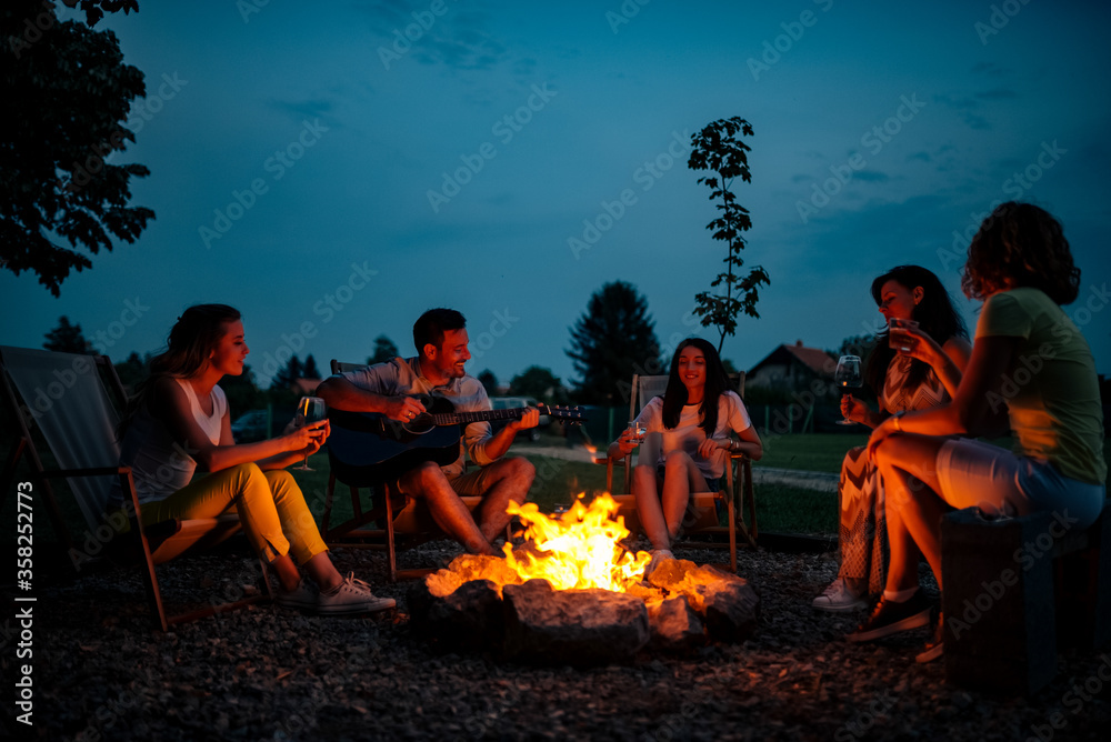 Playing guitar and singing around the bonfire at night. - obrazy, fototapety, plakaty 