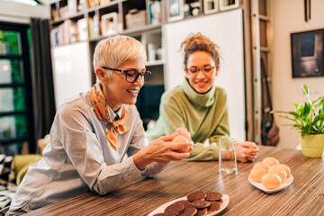 Wall Mural - Cheerful grandmother and granddaughter sitting at the table at home, portrait.