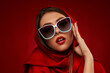 © producer - Portrait of chic brunette sexy girl with luxurious make-up in white sunglasses and red headscarf on red background
