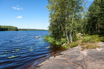 Wall Mural - Stony lake shore with green trees, the Saimaa Canal is near the Vyborg town, Russia. Horizontal image