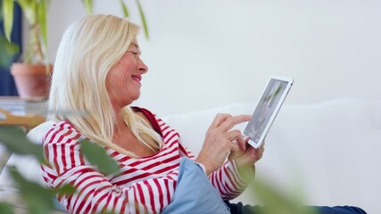 Wall Mural - Attractive senior woman with tablet sitting indoors on sofa, resting.