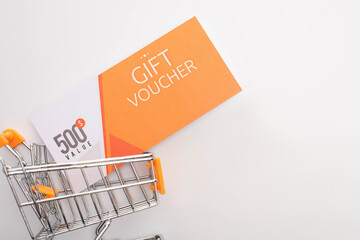 Wall Mural - Top view of gift voucher with value lettering in toy shopping cart on white background
