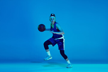 Wall Mural - Goal achievement. Young caucasian female basketball player training, prcticing with ball isolated on blue background in neon light. Concept of sport, movement, energy and dynamic, healthy lifestyle.