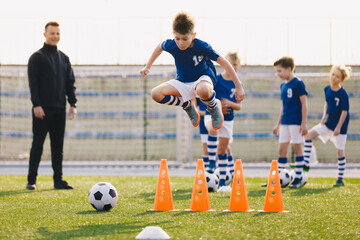 Wall Mural - Soccer school training unit. Football boys in team on practice session with youth coach. Player jumping over training cones on the grass field. Speed and agility soccer training