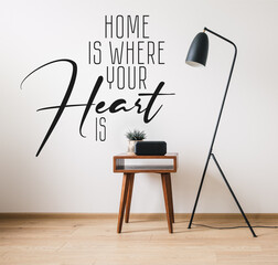 floor lamp and wooden coffee table with plant near clock with blank screen and home is where your heart is lettering