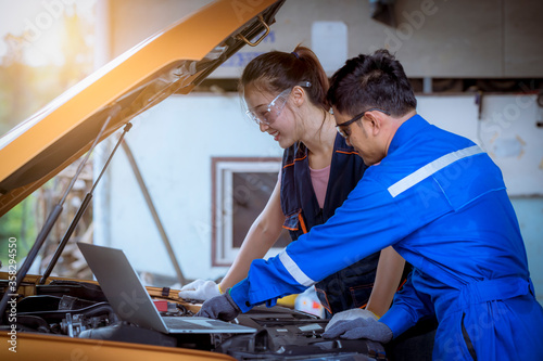 A man car mechanic under training woman to repairs and check car problem system check detail by laptop for maintenance and fixed in car garage.