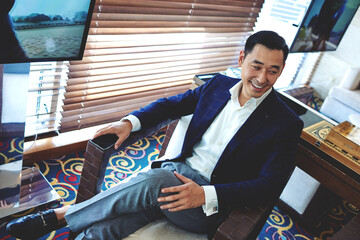 Cheerful smiling businessman sitting in modern restaurant resting after hard work day, happy asian men dressed in elegant suit enjoying free time, intelligent male entrepreneur relaxing in cafe