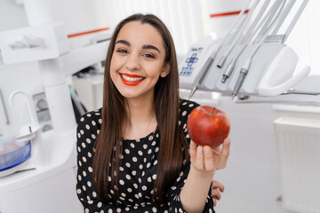 Wall Mural - Beautiful girl holds an apple at dentist`s office. Red apple at girl`s hands.