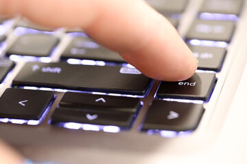 A closeup finger pushing the end button on an illuminated computer laptop keyboard