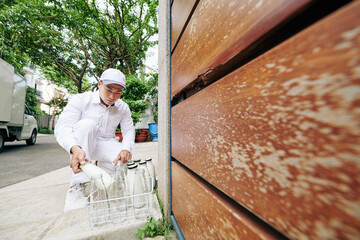 Wall Mural - Asian milkman in white uniform delivering milk in morning and taking empty glass bottles, copy space