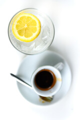 Glass of sparkling water with lemon and cup of coffee. Iced mineral water with lemon and cup of coffee on the white table.