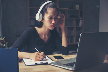 Wall Mural - Businesswoman working online at the home office by laptop. Asian young entrepreneurs watching webinars and talking during meeting video conferences call with team, Female writing agendar on book.