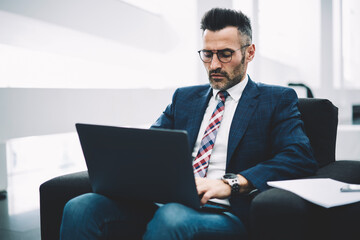 concentrated mature entrepreneur in formal wear working at modern lapto computer and checking mail v