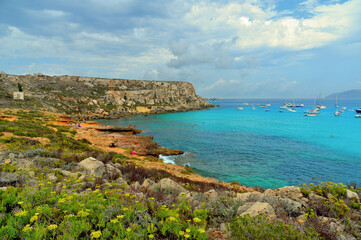 Wall Mural - paradise clear torquoise blue water with boats and cloudy blue sky in background in Favignana island, Cala Rossa Beach, Sicily South Italy.