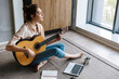 © Drobot Dean - Image of young woman writing notes while playing acoustic guitar at home