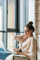 Image of focused woman working with laptop while sitting in armchair