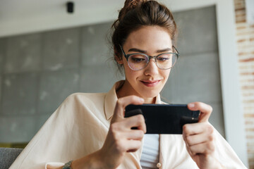 Wall Mural - Image of smiling attractive woman playing video game on mobile phone