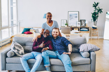 Wall Mural - Positive multiracial friends spending free time together at home interior showing thumb up sign, portrait of cheerful group of male and female hipsters n looking at camera gesture ok in living room