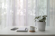 © paladin1212 - coffee cup with plant and notebook pen and phone on white desk with see through curtain