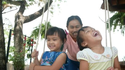 portrait of two pretty little girls and her mother playing with wooden swings in the garden happily.