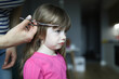 © H_Ko - Portrait of mother cutting of daughters bangs with metal scissors. Girl standing with sad expression. Hairdresser at home during lockdown. Family time together concept