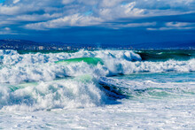 Storm Waves In White Foam Rush In Rows Along The Tsemesskaya Bay. Blue Sky And Green Sea. Dangerous And Dramatic. In The Background, Mountains, Multi-storey Buildings Of The City And Port.