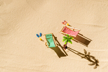 Aerial view of two deck chair, sunbed, lounge, glass of orange juice, flip flops, palm tree on sandy beach. Summer and travel concept. Minimalism