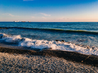 Wall Mural - View of the Black Sea, waves with sea foam, lit by sunlight at sunset, run ashore against the blue sea on a sunny evening.