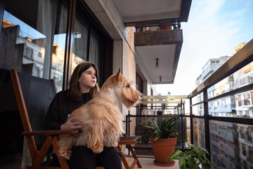 A Scottish Terrier dog is sitting on the lap of a pretty girl. On the balcony of a city house