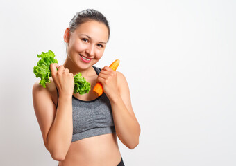 slender woman with a beautiful figure holds vegetables in her hands - carrots and lettuce