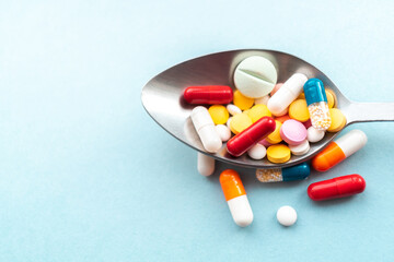 Assorted pills, tablets and pharmaceutical medicine capsules on a metallic spoon with blue background.