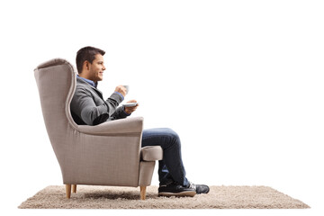 Wall Mural - Young man sitting in an armchair and drinking a cup of coffee