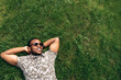 © Kateryna - Cheerful attractive afro american guy student resting while lying on a grass in the park at the university. Space for text