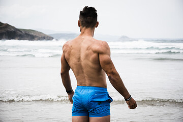 Young shirtless man with strong back at the beach 