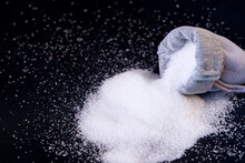 A Pile Of Sugar On Black Background, Granulated White Sugar And Cloth Bag