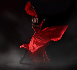 Flamenco woman spanish dancer in red dres performs with fan in dance at black background, studio shot