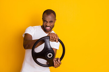 Photo of attractive dark skin guy man trying hard to turn car left right holding steering wheel driver wear casual white t-shirt isolated yellow vibrant color background