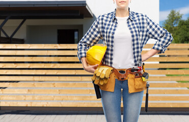 repair, construction and building concept - woman or builder with helmet and working tools on belt over living house background