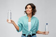 © Syda Productions - people concept - portrait of happy smiling young woman in turquoise shirt comparing water in plastic and reusable glass bottle grey background