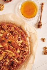 Poster - Vertical shot of a delicious apple walnut cake with honey surrounded by ingredients on a white table