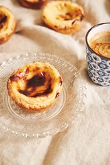 Canvas Print - Closeup shot of a delicious Portuguese egg tart on a plate with a cup of espresso on a white table